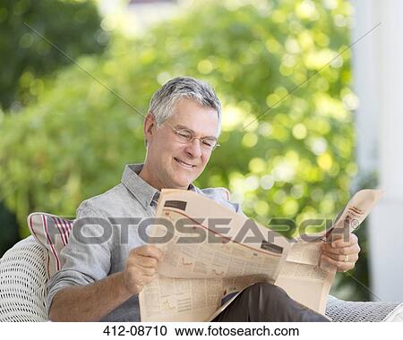 Stock Image - Senior man reading newspaper on patio. Fotosearch
