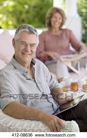 Senior man using digital tablet in armchair on patio View Large Photo Image Stock Photograph - Senior man using digital tablet in armchair on patio. Fotosearch