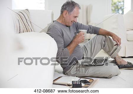 Stock Photo - Senior man using laptop on living room floor. Fotosearch