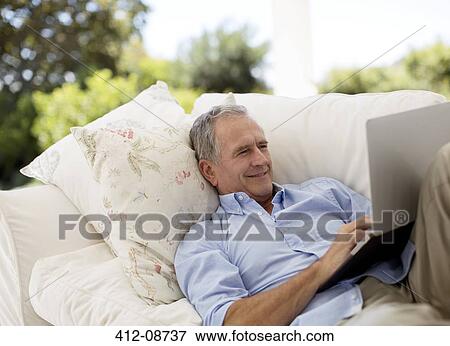 Senior man using laptop on patio sofa View Large Photo Image Stock Photo - Senior man using laptop on patio sofa. Fotosearch