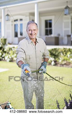 Senior man watering plants in garden View Large Photo Image Stock Image - Senior man watering plants in garden. Fotosearch