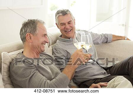 Stock Image - Senior men toasting wine glasses on sofa. Fotosearch