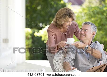 Stock Image - Senior woman bringing man cup of coffee on patio. Fotosearch