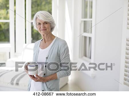 Senior woman holding cup of coffee in sun room View Large Photo Image Stock Photo - Senior woman holding cup of coffee in sun room. Fotosearch