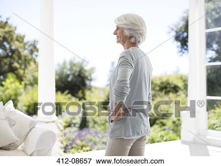 Stock Photo - Senior woman standing on patio. Fotosearch