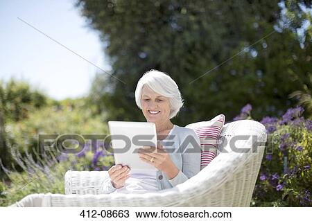Senior woman using digital tablet in armchair View Large Photo Image Stock Image - Senior woman using digital tablet in armchair. Fotosearch