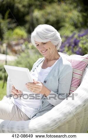 Stock Photo - Senior woman using digital tablet in armchair. Fotosearch