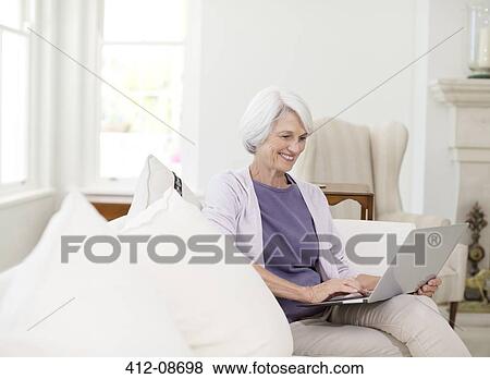 Senior woman using laptop on sofa in living room View Large Photo Image Stock Photo - Senior woman using laptop on sofa in living room. Fotosearch