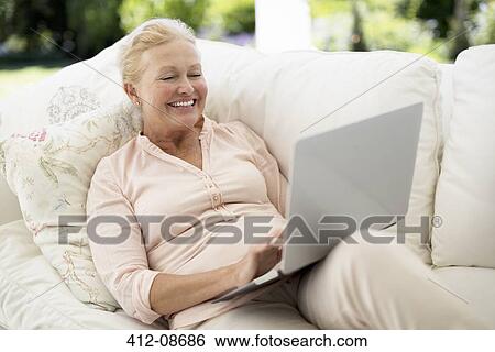 Stock Photograph - Senior woman using laptop on sofa. Fotosearch
