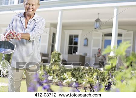 Senior woman watering plants in garden View Large Photo Image Stock Image - Senior woman watering plants in garden. Fotosearch