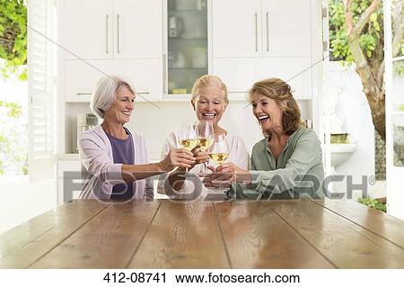 Stock Image - Senior women toasting wine glasses in kitchen. Fotosearch