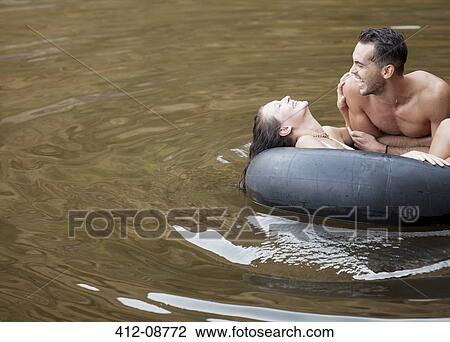 Stock Image - Couple playing in inner tube on lake. Fotosearch