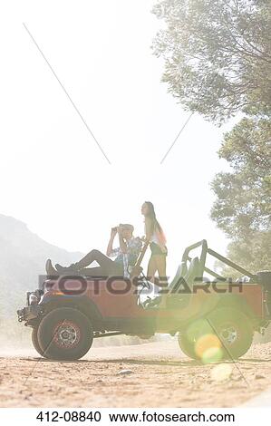 Stock Image - Couple relaxing in sport utility vehicle on dirt road. Fotosearch