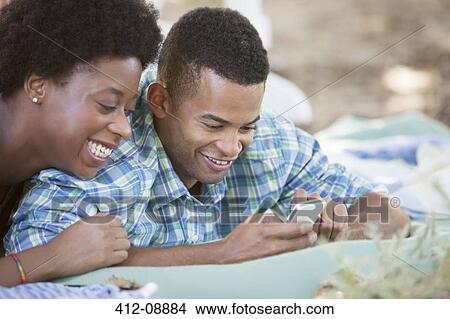 Couple using cell phone on blanket View Large Photo Image Picture - Couple using cell phone on blanket. Fotosearch