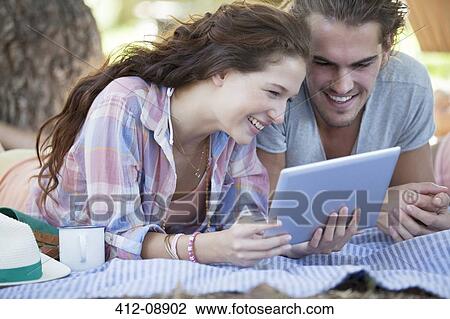 Stock Image - Couple using digital tablet on blanket outdoors. Fotosearch