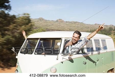 Stock Photo - Man leaning head out camper van window on rural road. Fotosearch