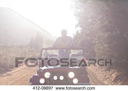 Stock Photo - Man standing in sport utility vehicle on dirt road. Fotosearch