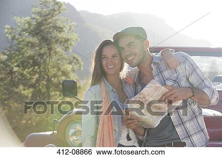 Stock Photograph - Smiling couple with map next to sport utility vehicle. Fotosearch