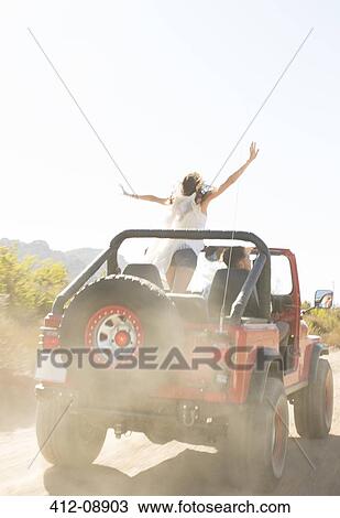 Stock Image - Woman cheering in sport utility vehicle on dirt road. Fotosearch
