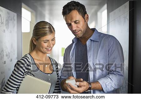 Business people looking down at cell phone in corridor View Large Photo Image Stock Image - Business people looking down at cell phone in corridor. Fotosearch
