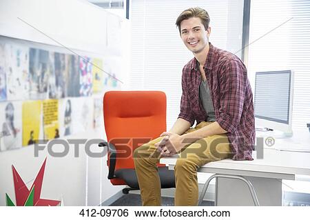 Businessman sitting on desk in office View Large Photo Image Stock Photograph - Businessman sitting on desk in office. Fotosearch