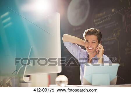 Stock Photography - Businessman talking on cell phone at desk in office. Fotosearch