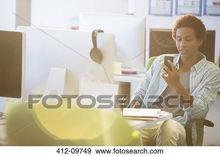 Stock Photo - Businessman using cell phone at desk in office. Fotosearch