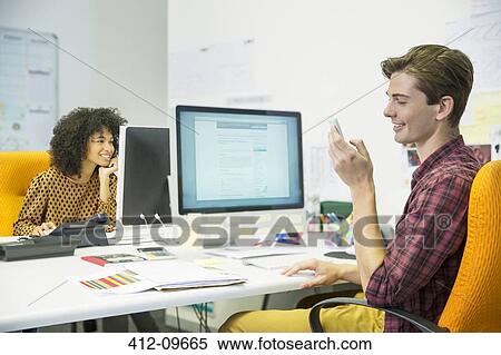 Stock Photography - Businessman using cell phone at desk in office. Fotosearch