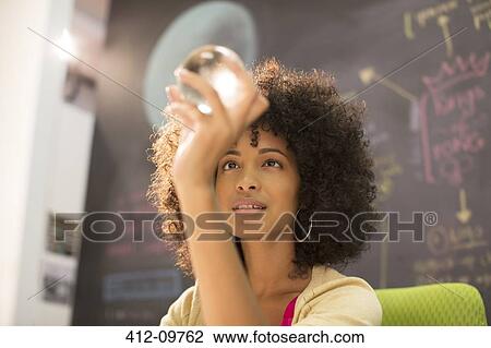 Stock Image - Businesswoman examining crystal ball in office. Fotosearch
