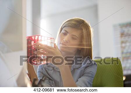 Stock Image - Businesswoman examining cube at desk in office. Fotosearch