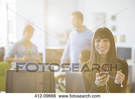 Businesswoman listening to mp3 player in office View Large Photo Image Stock Photograph - Businesswoman listening to mp3 player in office. Fotosearch