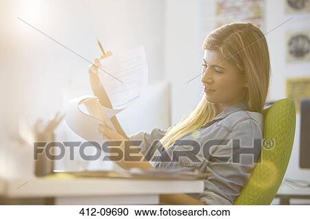 Stock Image - Businesswoman reading at desk in office. Fotosearch
