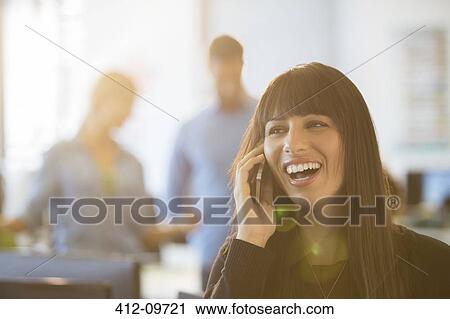 Stock Image - Businesswoman talking on cell phone in office. Fotosearch