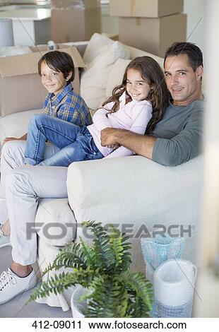 Stock Image - Father and children relaxing on sofa among cardboard boxes. Fotosearch
