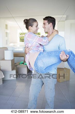 Stock Image - Man carrying girlfriend in new house. Fotosearch
