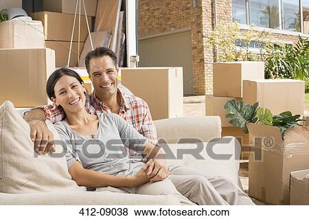 Stock Photo - Portrait of smiling couple on sofa near moving van in driveway. Fotosearch