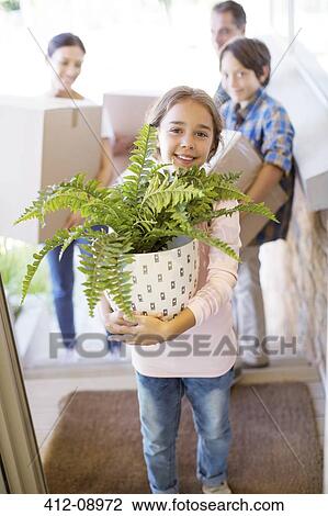 Stock Image - Portrait of smiling family moving belongings into house. Fotosearch