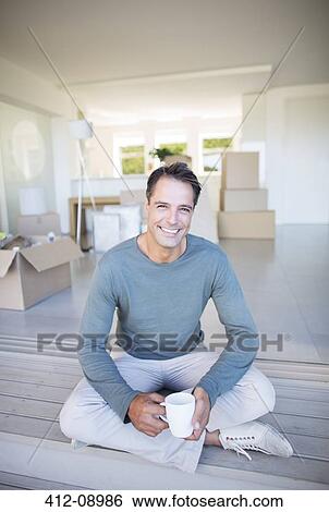 Stock Photograph - Portrait of smiling man drinking coffee among cardboard boxes. Fotosearch