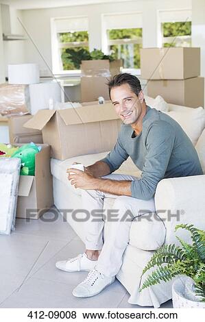 Portrait of smiling man enjoying coffee on sofa among cardboard boxes View Large Photo Image Stock Photo - Portrait of smiling man enjoying coffee on sofa among cardboard boxes. Fotosearch
