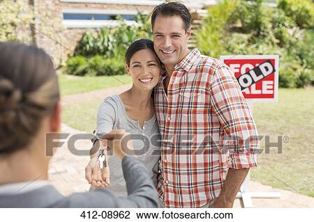 Stock Image - Realtor giving couple keys to new house. Fotosearch