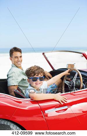 Boy sitting behind steering wheel of convertible with father at beach View Large Photo Image Stock Photo - Boy sitting behind steering wheel of convertible with father at beach. Fotosearch