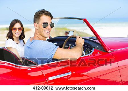 Stock Image - Couple driving convertible on beach. Fotosearch
