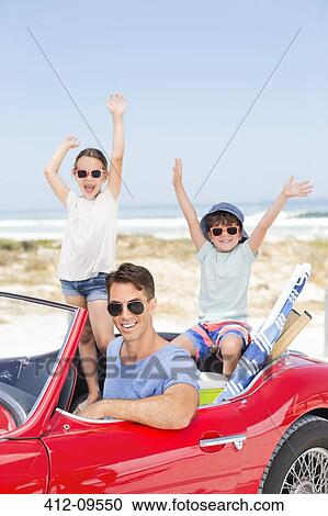 Stock Image - Father and children in convertible at beach. Fotosearch