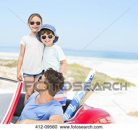 Stock Image - Father and children smiling in convertible at beach. Fotosearch