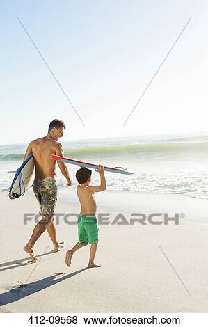 Stock Photo - Father and son carrying surfboard and bodyboard on beach. Fotosearch