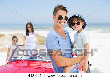 Stock Photo - Father and son smiling near convertible on beach. Fotosearch