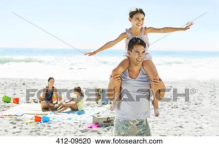 Stock Image - Father carrying daughter on shoulders at beach. Fotosearch