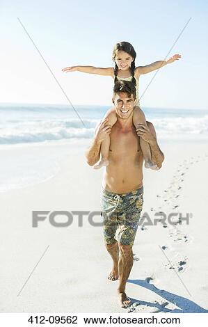 Stock Image - Father carrying daughter on shoulders at beach. Fotosearch