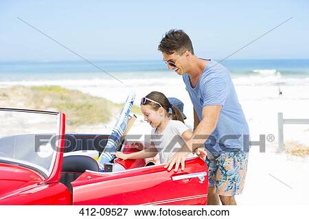 Stock Photo - Father helping daughter into convertible on beach. Fotosearch