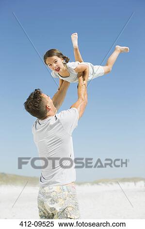 Stock Photography - Father lifting daughter overhead on beach. Fotosearch